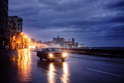 Car on wet road in city against sky at dusk