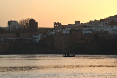 Buildings by sea against clear sky during sunset