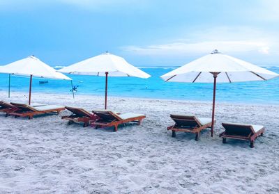 Deck chairs on beach against sky