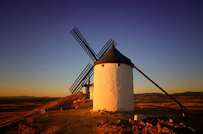 Traditional windmill on field against clear sky during sunset