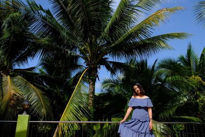 Portrait of young woman standing on palm tree