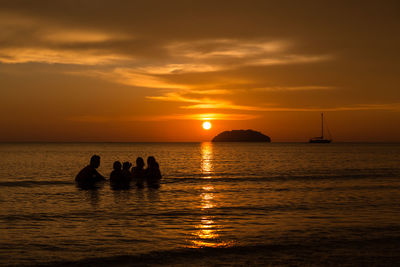 Silhouette people on sea against sky during sunset