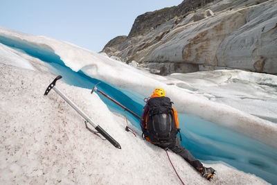 Man sitting by glacier against mountains