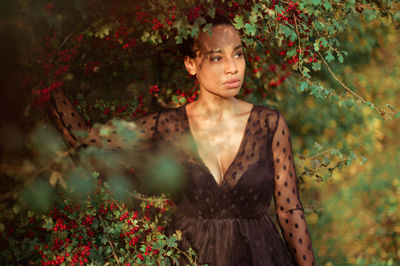 Young woman looking away while standing against plants