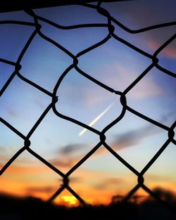 Low angle view of chainlink fence against sky during sunset