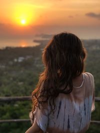 Rear view of woman standing against sea during sunset