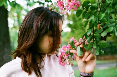 Young woman touching flowers while standing at park