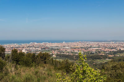 Aerial view of townscape by sea against blue sky