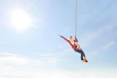 Low angle view of carefree teenage girl standing on rope against sky