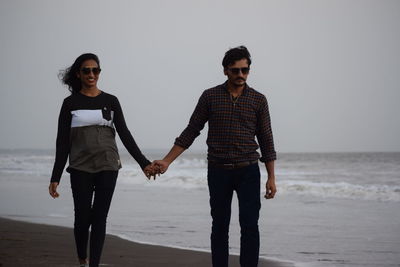 Couple holding hands while walking on shore at beach