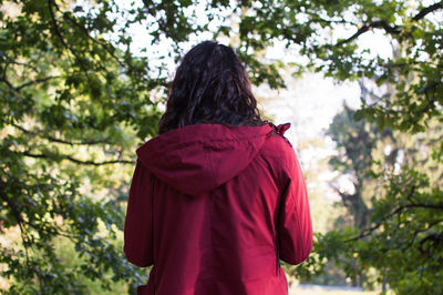 Rear view of woman wearing hooded jacket while standing against trees