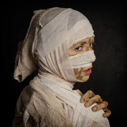 Rear view of woman wearing mummy costume standing against black background