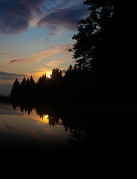 Silhouette trees by lake against sky during sunset