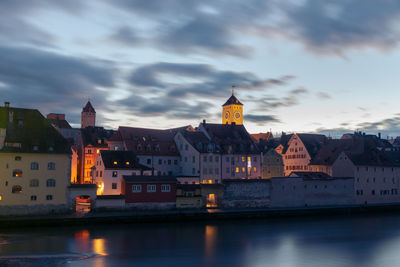 Buildings at waterfront against cloudy sky