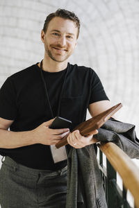 Portrait of smiling male professional standing with mobile phone and file at convention center