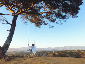 Rear view of woman swinging over on mountain against sky