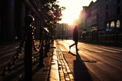 Silhouette man walking in city against sky during sunset