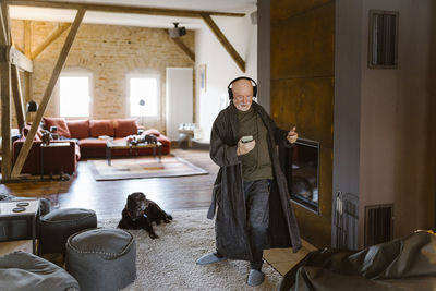 Carefree senior man dancing and listening to music while standing on carpet at home