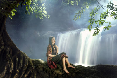Young woman sitting by waterfall in forest