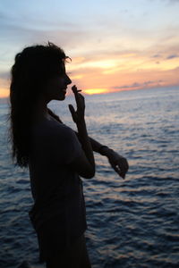 Side view of woman smoking while standing at beach during sunset