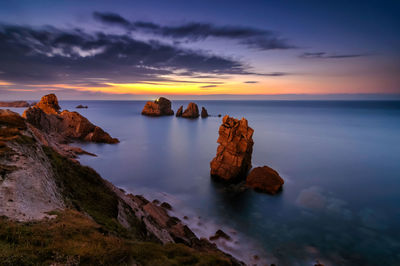 Rocks in sea against sky during sunset