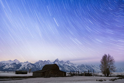 Barn on snow covered field against star trails at dusk