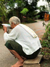 Side view of senior man holding container while sitting on street