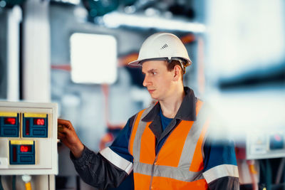 Operator or engineer in helmet and protective vest checks modern equipment in industrial plant