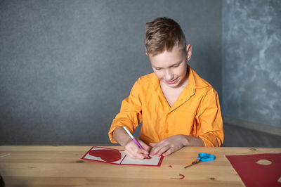 Cute boy cuts out a valentine's day card with hearts. a boy in a bright shirt