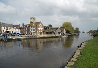 Buildings by river against sky