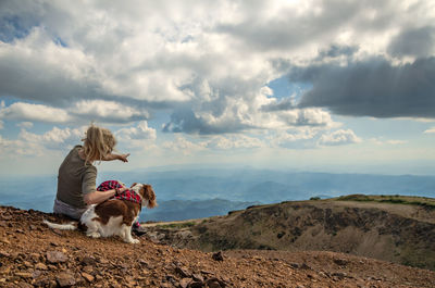 Woman and her dog, cavalier king charles spaniel, on a mountain top watching a picturesque landscape