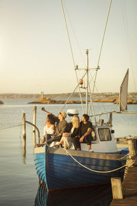 Young man taking selfie with friends while sitting on boat moored at harbor