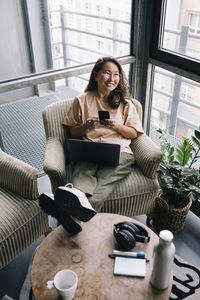 Happy computer programmer with laptop and smart phone sitting in chair at office