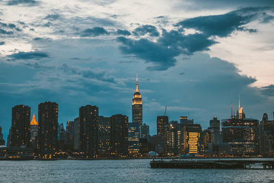 Illuminated buildings in city against cloudy sky