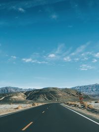 Road by mountains against blue sky