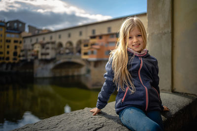 Portrait of smiling girl against water, in front of medieval bridge, ponte vecchio, florenz italy