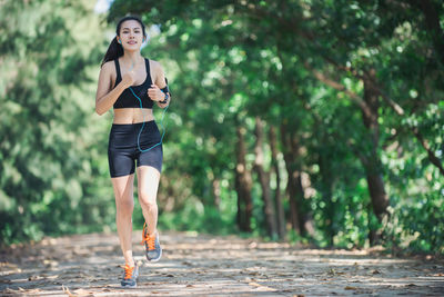 Full length portrait of determined young woman jogging on road amidst trees