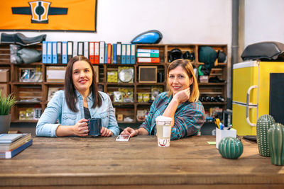 Portrait of two smiling female entrepreneurs looking at camera behind of counter in motorbike shop