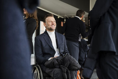 Smiling disabled businessman sitting in wheelchair looking at male delegate during seminar