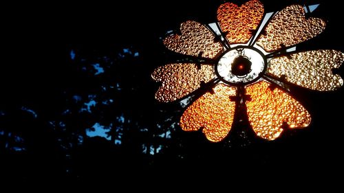 Low angle view of illuminated light bulb hanging against black background