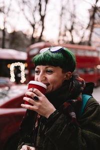 Happy non-binary hipster drinking coffee while walking on city street