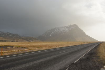 Country road by mountains against sky