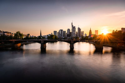 Bridge over river in city during sunset