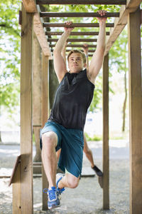 Full length of determined man hanging on monkey bars at outdoor gym