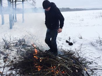 Full length of senior man standing by burning fire on snow covered land