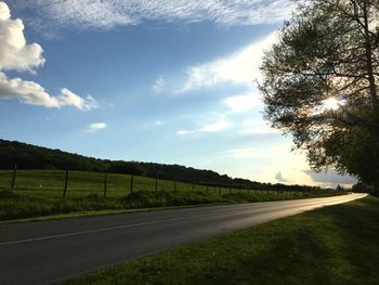 Country road amidst field against sky
