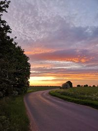 Road amidst field against sky during sunset