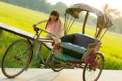 Portrait of girl sitting by field on pedicab