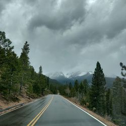 Empty road amidst trees against cloudy sky