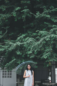 Portrait of young woman holding umbrella standing against trees